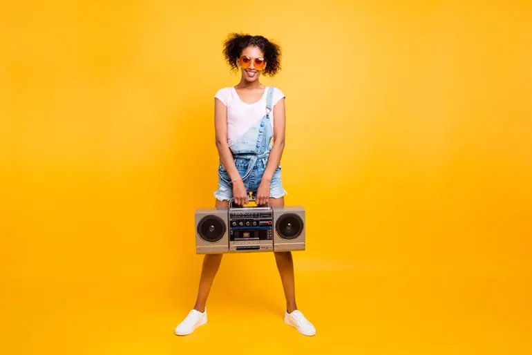 A Beautiful black woman smiles on a yellow background holding a Boombox