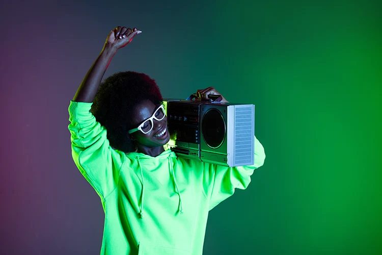 A Beautiful dark skin woman with natural hair smile holding a boombox on a gradient green background. Inspir3 Live.
