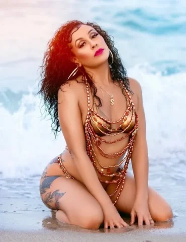 A beautiful woman poses in a beach in a gold bikini her name is Sylina Renae