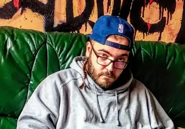 A White man stares at the camera DJ King Flow wearing a blue baseball cap toward backwards, glasses and hoodie. For Mixtape Addict.